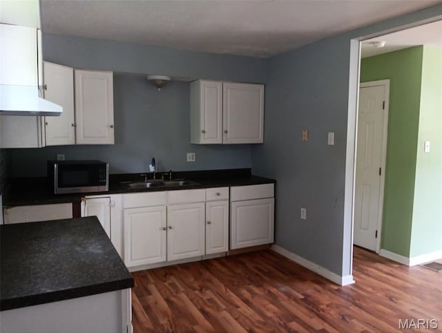 4664 Pogue Dr, House Springs, MO 63051 - kitchen with stainless steel microwave, white cabinetry, dark wood-style flooring, under cabinet range hood, and dark countertops