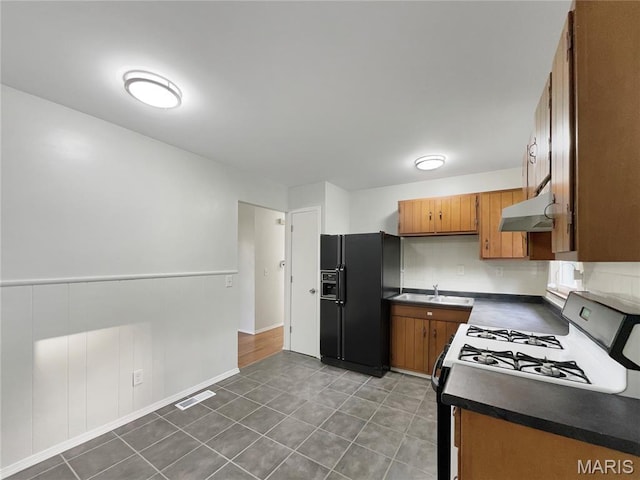 5031 Tulip Tree Ln, Hazelwood, MO 63042 - kitchen with black refrigerator with ice dispenser, range with gas stovetop, under cabinet range hood, dark countertops, and brown cabinets