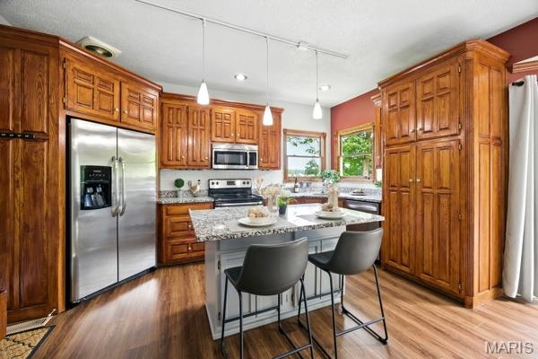 5 Sherman Ct, Hillsboro, MO 63050 - kitchen featuring appliances with stainless steel finishes, brown cabinetry, light stone countertops, wood finished floors, and hanging light fixtures
