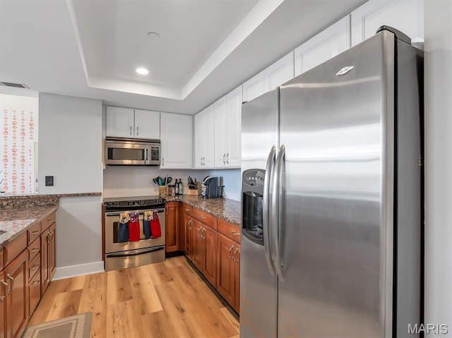 314 N Broadway Unit 1107, Saint Louis, MO 63102 - kitchen featuring stainless steel appliances, light wood-style flooring, dark stone countertops, brown cabinets, and a raised ceiling