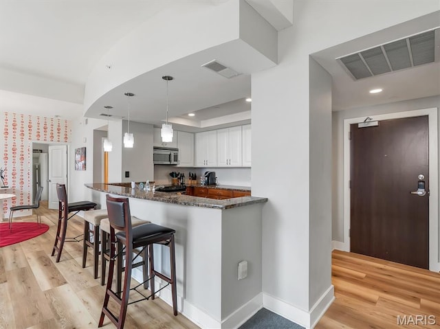 314 N Broadway Unit 1107, Saint Louis, MO 63102 - kitchen with stainless steel microwave, a breakfast bar area, light wood finished floors, dark stone countertops, and white cabinetry