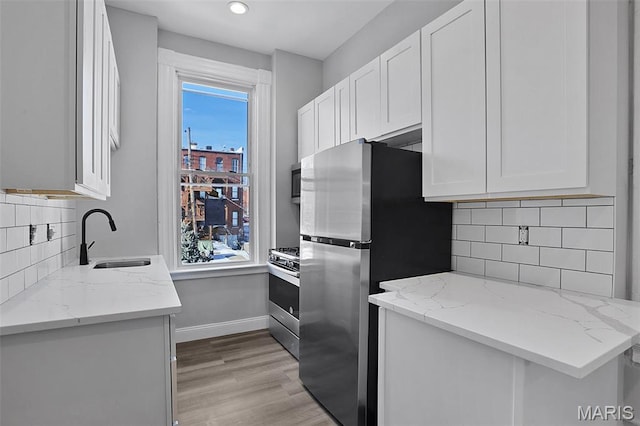 2205 S 11th St, Saint Louis, MO 63104 - kitchen with appliances with stainless steel finishes, light stone countertops, white cabinets, light wood-style floors, and decorative backsplash