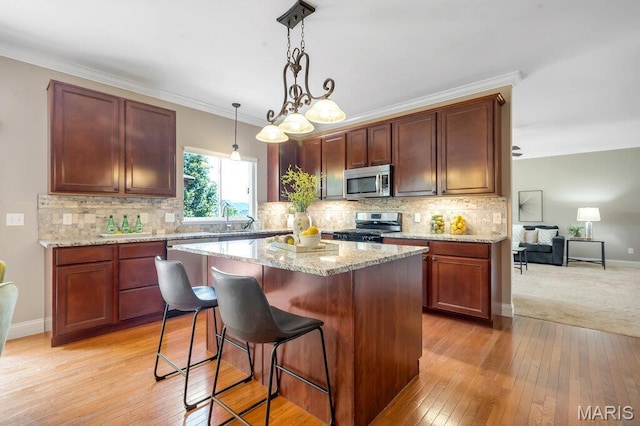 714 Oriental Lily Dr, Ofallon, MO 63366 - kitchen featuring appliances with stainless steel finishes, backsplash, a kitchen island, a breakfast bar area, and ornamental molding
