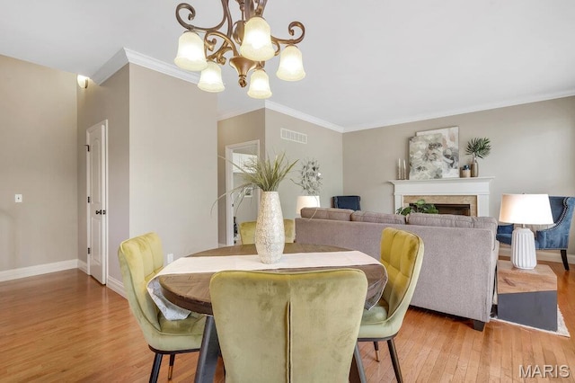 714 Oriental Lily Dr, Ofallon, MO 63366 - dining room featuring light wood-style flooring, a chandelier, crown molding, and a fireplace