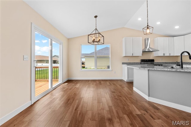 225 Ranchero Dr, Hamel, IL 62046 - kitchen featuring wall chimney range hood, white cabinets, lofted ceiling, wood finished floors, and light stone counters