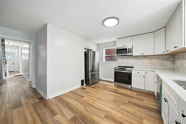 4550 Enright Ave, Saint Louis, MO 63108 - kitchen with stainless steel appliances, light countertops, decorative backsplash, light wood finished floors, and white cabinets