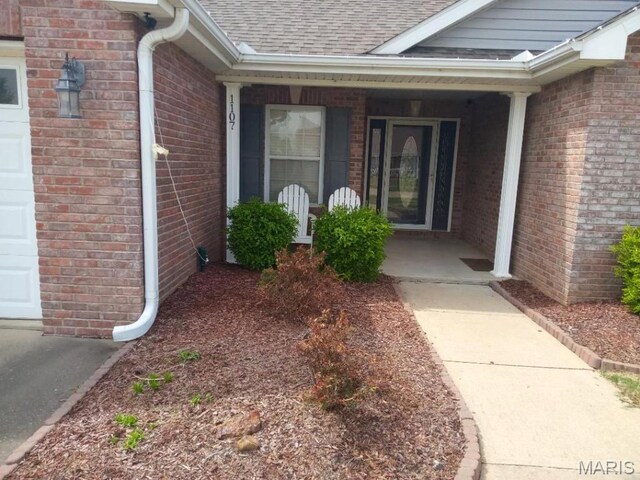 1107 Daffodil St, Sikeston, MO 63801 - doorway to property with a shingled roof, covered porch, brick siding, and a garage