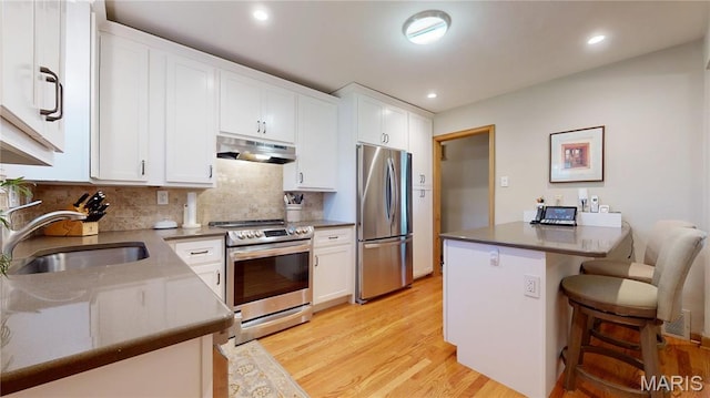 9334 Litzsinger Rd, Rock Hill, MO 63144 - kitchen featuring stainless steel appliances, under cabinet range hood, white cabinetry, a breakfast bar area, and recessed lighting