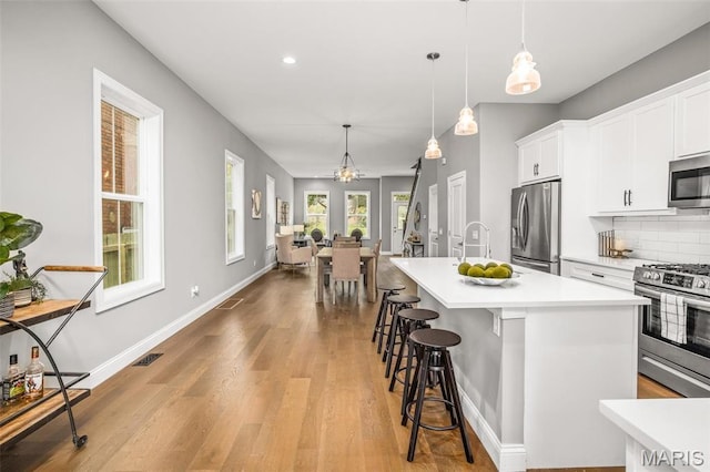 3400 Vista Ave, Saint Louis, MO 63104 - kitchen featuring appliances with stainless steel finishes, light wood-type flooring, light countertops, backsplash, and a kitchen island with sink