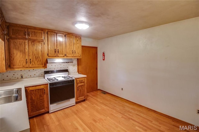 6155 Raymond Rd, Bunker Hill, IL 62014 - kitchen with white range with gas cooktop, under cabinet range hood, light wood-style flooring, backsplash, and light countertops
