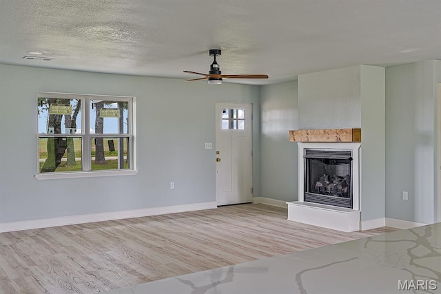 3120 State Highway F, Cardwell, MO 63829 - unfurnished living room with light wood-style flooring, a fireplace with raised hearth, a ceiling fan, and a textured ceiling