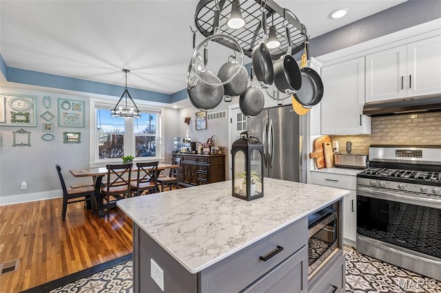 402 S Walker St, Montgomery City, MO 63361 - kitchen featuring appliances with stainless steel finishes, under cabinet range hood, white cabinetry, decorative backsplash, and wood finished floors