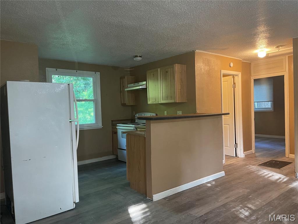 38 Westdell Dr, Dellwood, MO 63136 - kitchen with white appliances, under cabinet range hood, dark wood finished floors, a textured ceiling, and a peninsula