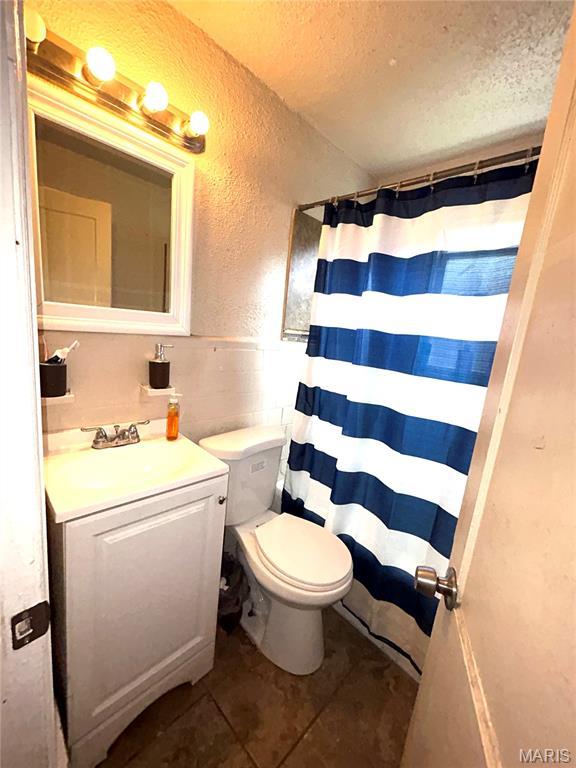 7155 Theodore Ave, Jennings, MO 63136 - bathroom with tile patterned floors, a textured ceiling, vanity, a textured wall, and curtained shower