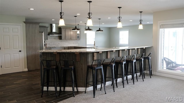 3215 Timber Ridge Rd, Palmyra, MO 63461 - kitchen with wall chimney range hood, a breakfast bar, recessed lighting, decorative backsplash, and light stone countertops