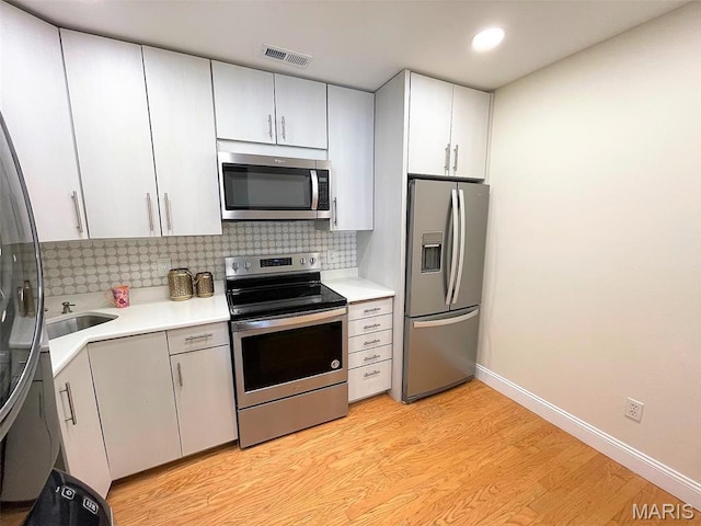 1418 Bluebird Ter, Saint Louis, MO 63144 - kitchen with stainless steel appliances, light countertops, light wood-style flooring, tasteful backsplash, and recessed lighting