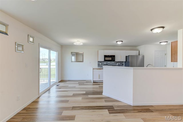 502 Summer Glen Ln, Saint Charles, MO 63301 - kitchen featuring freestanding refrigerator, black microwave, white cabinets, and light wood finished floors