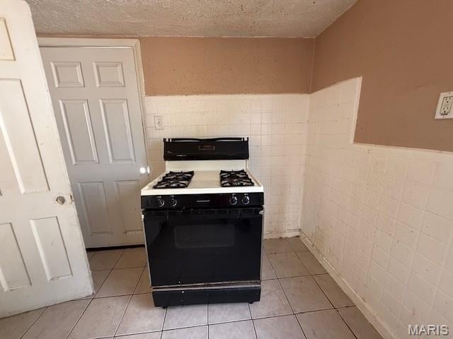 7446 Calvin Ave, Country Club Hills, MO 63136 - kitchen with gas range, a textured ceiling, light tile patterned flooring, tile walls, and wainscoting
