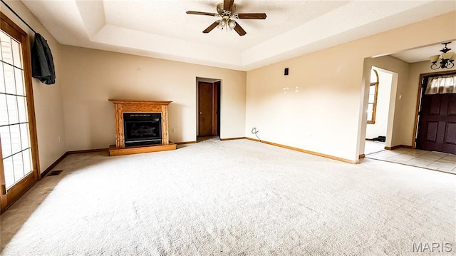 200 April Dr, Saint Robert, MO 65584 - unfurnished living room with carpet floors, a glass covered fireplace, a ceiling fan, a tray ceiling, and a chandelier