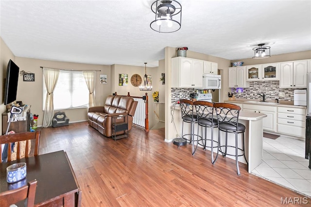 7800 Chuck Ct, Godfrey, IL 62035 - kitchen with white microwave, a kitchen breakfast bar, backsplash, and white cabinetry