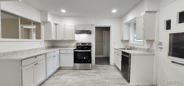 115 N 5th St, De Soto, MO 63020 - kitchen with appliances with stainless steel finishes, under cabinet range hood, light countertops, recessed lighting, and white cabinets