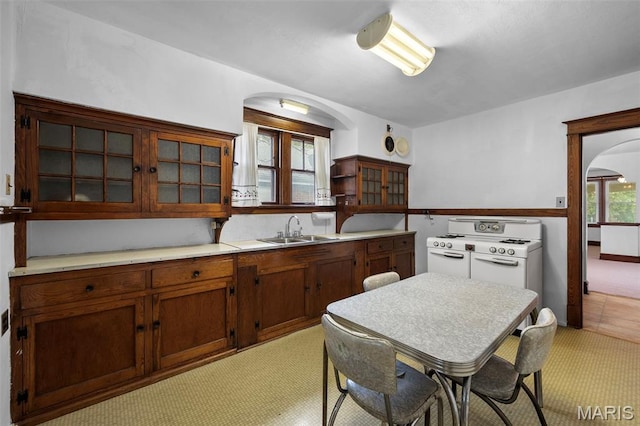 887 Wall St, Saint Louis, MO 63147 - kitchen featuring arched walkways, gas range gas stove, light colored carpet, light countertops, and glass insert cabinets
