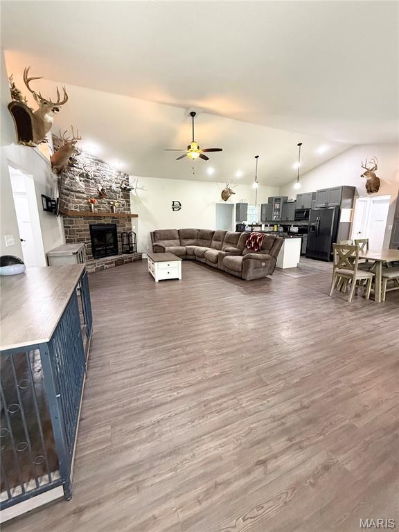 22115 Royce Ln, Waynesville, MO 65583 - living room featuring wood finished floors, a ceiling fan, vaulted ceiling, and a stone fireplace