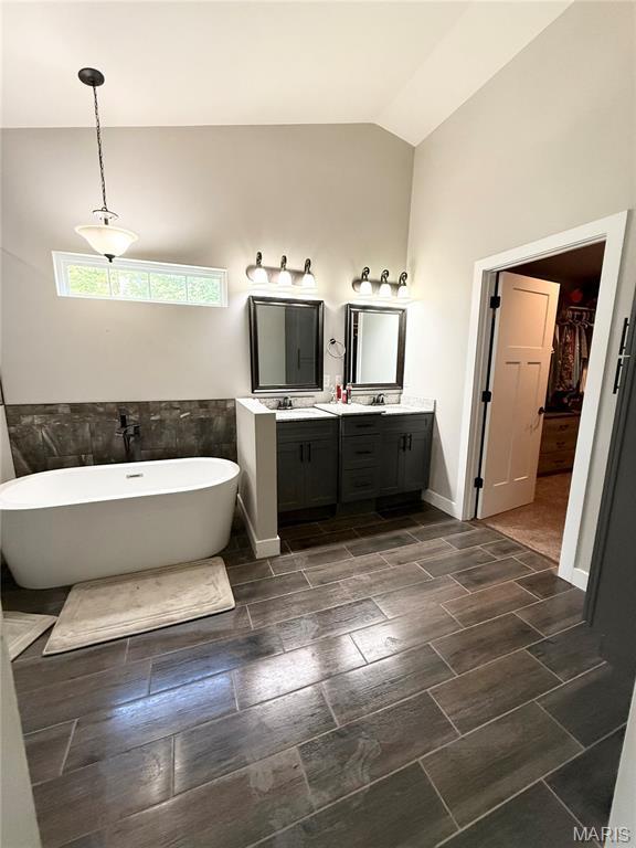 22115 Royce Ln, Waynesville, MO 65583 - bathroom featuring double vanity, a soaking tub, vaulted ceiling, a walk in closet, and tile walls