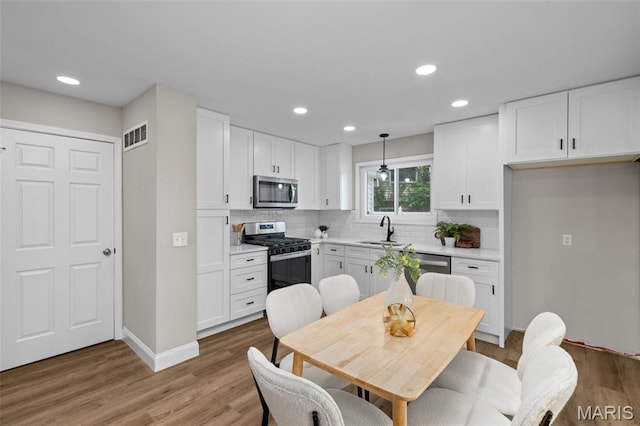 145 Aspencade Cir, Saint Peters, MO 63376 - kitchen with appliances with stainless steel finishes, white cabinetry, backsplash, light wood-style flooring, and recessed lighting