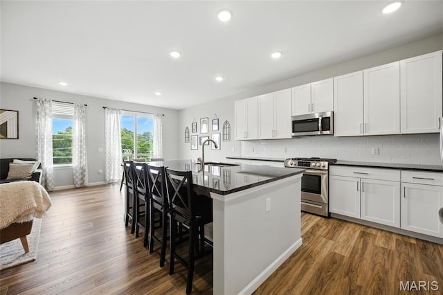 213 Dell View Dr, Arnold, MO 63010 - kitchen with stainless steel appliances, a kitchen island with sink, a kitchen breakfast bar, wood finished floors, and recessed lighting