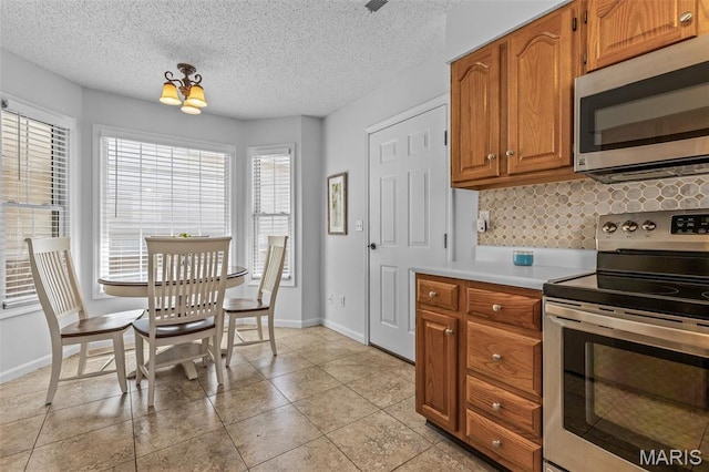 1531 Charmaine Dr, Bonne Terre, MO 63628 - kitchen featuring appliances with stainless steel finishes, backsplash, light countertops, brown cabinets, and a textured ceiling