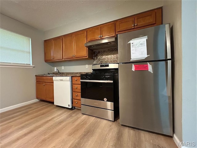 6023 Shillington Dr, Berkeley, MO 63134 - kitchen with stainless steel appliances, under cabinet range hood, light wood-style floors, brown cabinets, and decorative backsplash