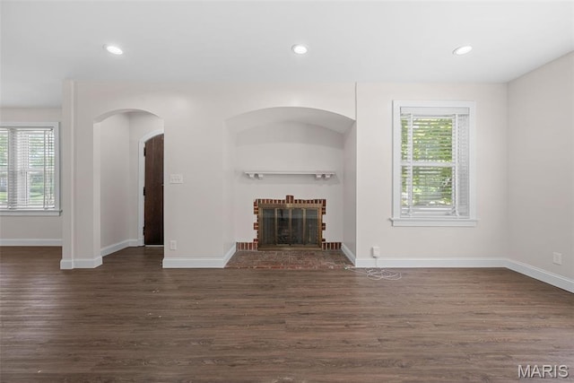 8260 Glen Echo Dr, Bel-Nor, MO 63121 - unfurnished living room featuring plenty of natural light, dark wood-style flooring, recessed lighting, a brick fireplace, and arched walkways
