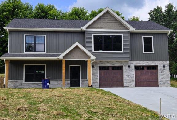 31571 Mimosa Ct, Foristell, MO 63348 - view of front facade featuring covered porch, stone siding, a front lawn, and an attached garage