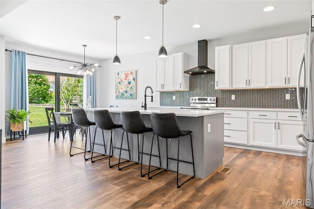 10523 Village Ln, Foristell, MO 63348 - kitchen featuring wall chimney exhaust hood, appliances with stainless steel finishes, a chandelier, a center island with sink, and backsplash