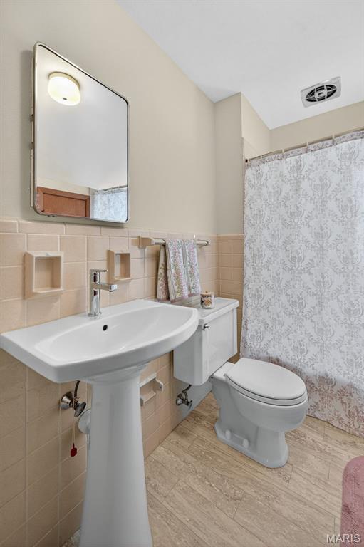 6580 Oleatha Ave, Saint Louis, MO 63139 - full bathroom with tile walls, wood finished floors, a shower with curtain, and wainscoting