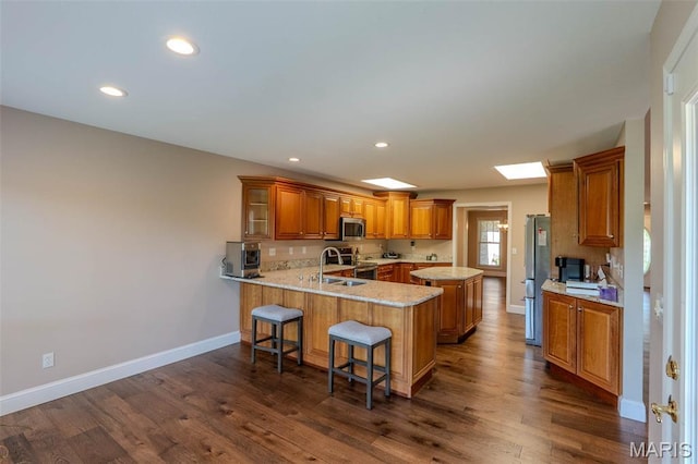 11782 Pine Forest Dr, Rolla, MO 65401 - kitchen with appliances with stainless steel finishes, a peninsula, brown cabinetry, a breakfast bar, and dark wood-style floors
