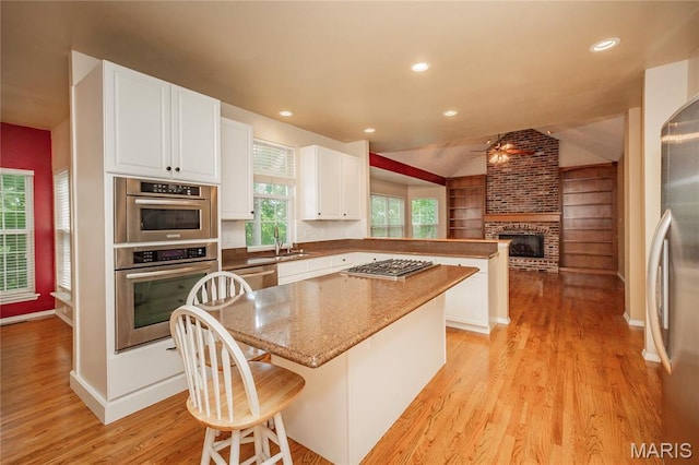 742 Arbor Ridge Ct, Ballwin, MO 63021 - kitchen featuring appliances with stainless steel finishes, a ceiling fan, a peninsula, a brick fireplace, and light wood-style flooring