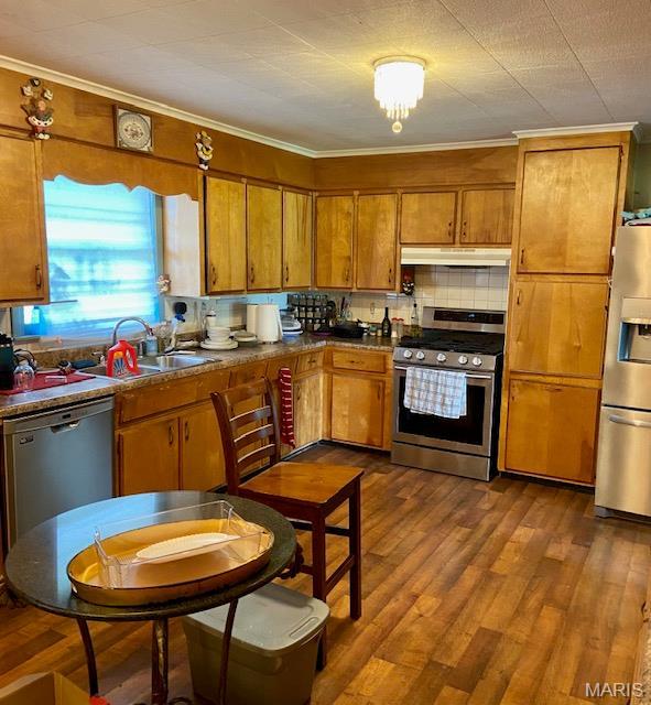 kitchen with stainless steel appliances, under cabinet range hood, brown cabinets, ornamental molding, and dark wood-style flooring