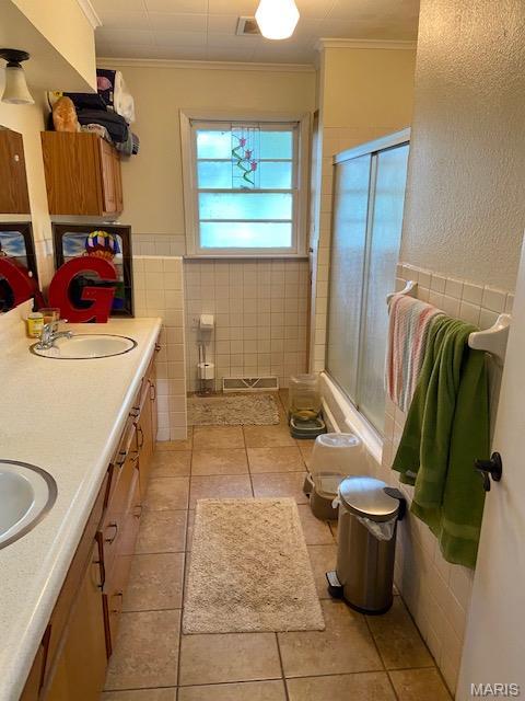 full bath featuring crown molding, tile walls, a shower with shower door, tile patterned floors, and double vanity