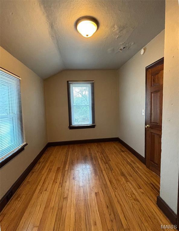 9758 Diamond Dr, Riverview, MO 63137 - empty room with light wood-style flooring, a textured ceiling, vaulted ceiling, and a smoke detector