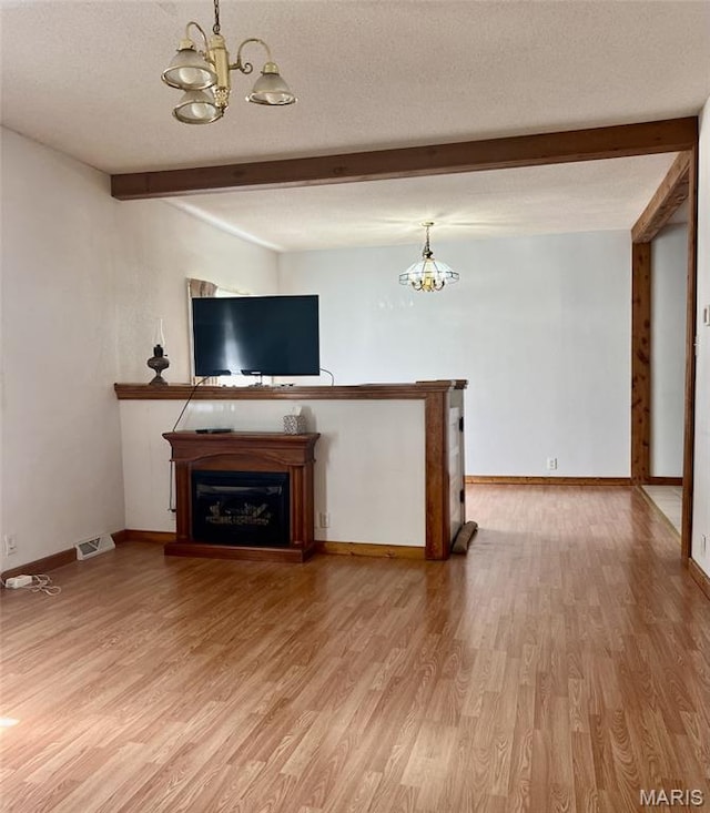 315 E N St, Saint Clair, MO 63077 - unfurnished living room with a chandelier, beamed ceiling, light wood-style flooring, a textured ceiling, and a glass covered fireplace