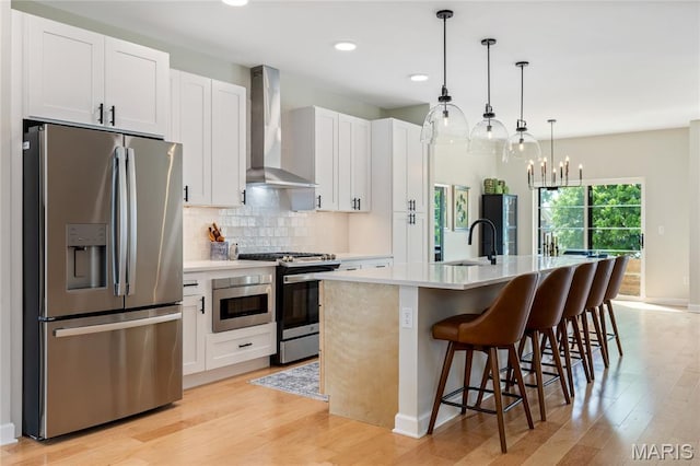 6297 Magnolia Ave, Saint Louis, MO 63139 - kitchen with appliances with stainless steel finishes, wall chimney exhaust hood, a center island with sink, light wood finished floors, and light countertops