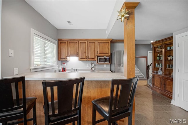 2175 Oberhelman Rd, Foristell, MO 63348 - kitchen with stainless steel appliances, brown cabinetry, a kitchen breakfast bar, light countertops, and a peninsula