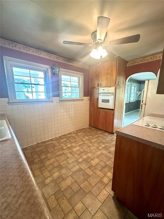 701 Alvarado, Belle, MO 65013 - kitchen with white appliances, ceiling fan, wainscoting, arched walkways, and tile walls