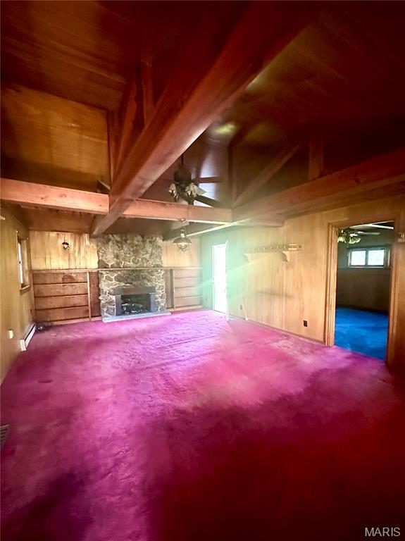 701 Alvarado, Belle, MO 65013 - unfurnished living room featuring carpet flooring, wooden walls, a baseboard heating unit, a stone fireplace, and a ceiling fan