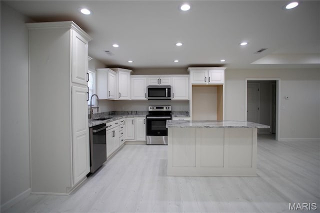 1205 Yosemite, Sikeston, MO 63801 - kitchen featuring appliances with stainless steel finishes, white cabinets, a center island, light wood-style flooring, and light stone counters