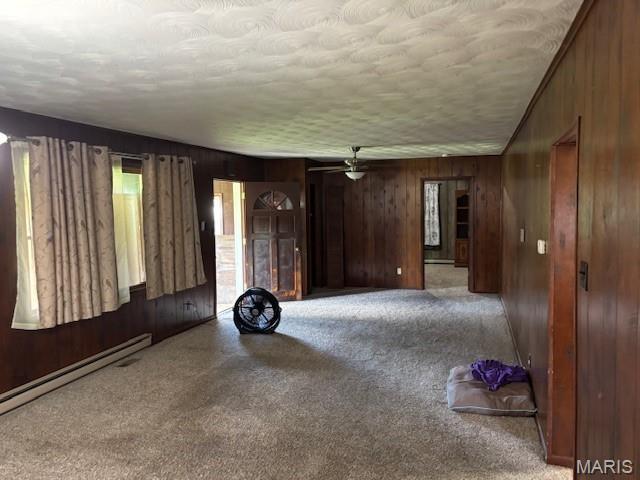 304 Taylor Ave, Park Hills, MO 63601 - unfurnished living room featuring carpet, wooden walls, a ceiling fan, a baseboard radiator, and a textured ceiling