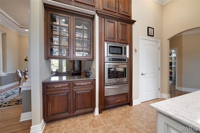 204 Logans Ct, Foristell, MO 63348 - kitchen featuring a warming drawer, appliances with stainless steel finishes, arched walkways, glass insert cabinets, and crown molding