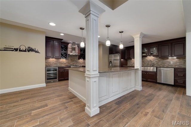 204 Logans Ct, Foristell, MO 63348 - kitchen with wine cooler, appliances with stainless steel finishes, decorative columns, wall chimney range hood, and backsplash